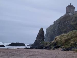 a beach with a lighthouse on top of a mountain at The Apartment Benone in Castlerock +3 photos