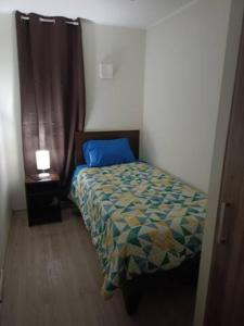 ein kleines Schlafzimmer mit einem Bett mit einem blauen Kissen in der Unterkunft Habitaciones en Departamento Centro de Chillan in Chillán