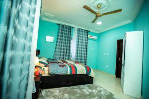a bedroom with blue walls and a bed with a ceiling fan at Matata Homes Airbnb in Kasoa