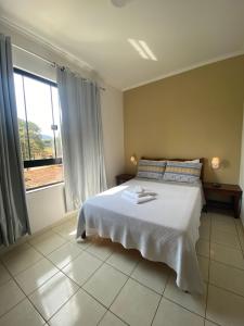 um quarto com uma cama branca e uma grande janela em Pousada da Mariinha em São Lourenço