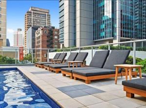 a row of lounge chairs on a rooftop with a pool at Comfy 2B1B CBD Riverview apt w Parking+Pool+Gym in Brisbane
