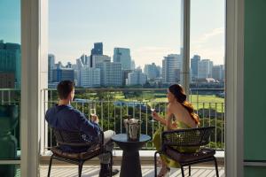 a man and woman sitting on a balcony with a view of a city at Dusit Suites Hotel Ratchadamri, Bangkok in Bangkok