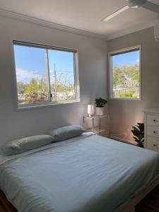 a bedroom with a large bed with two windows at Casa de Palmas Noosa in Noosaville