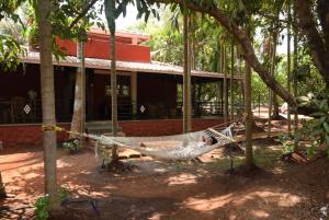 a man laying in a hammock in front of a house at Red Roof Farmhouse in Chiplun