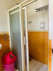 a bathroom with a shower door and a pink trash can at Highland Beach Apartments Goa in Baga