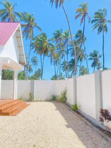 een wit hek met palmbomen op de achtergrond bij Nakupenda House in Jambiani
