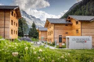 a row of wooden buildings with mountains in the background at SWISSPEAK Resorts by Pierre & Vacances Premium Zinal in Zinal