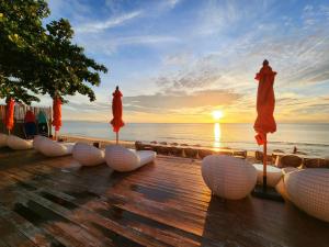 a wooden deck with umbrellas on the beach with the sunset at Yotaka Khanom in Ban Phang Phrao
