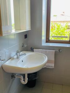 lavabo blanco en un baño con ventana en Foresteria Miramonti affittacamere, en Fiavè