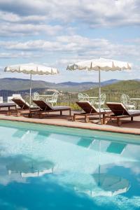 a swimming pool with two chairs and umbrellas at Borgo Vescine in Radda in Chianti