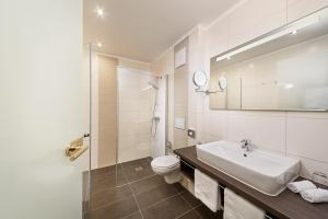 a white bathroom with a toilet and a sink at Ringhotel Sonneck in Bad Wörishofen