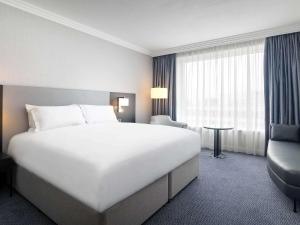 um quarto de hotel com uma grande cama branca e uma cadeira em Sofitel London Gatwick em Horley