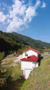 ein weißes Gebäude mit rotem Dach auf einem Hügel in der Unterkunft Къща за гости ДАП Баните in Banite