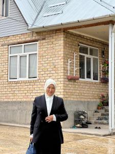 Una donna con un hijab in piedi davanti a una casa di Jyrgal jashoo guest house 