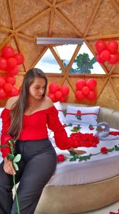 una mujer sentada en una cama sosteniendo rosas en Magia Verde Glamping, en Tinjacá