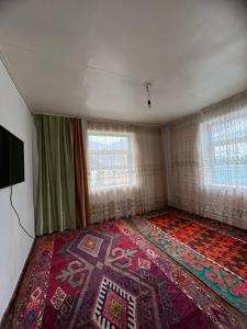 Cette chambre comprend un lit avec un tapis et 2 fenêtres. dans l'établissement Ata konush, à Sufi-Kurgan