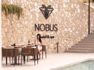 a woman sitting at a table in front of a stone wall at Nobus Hotel & Spa in Vlorë