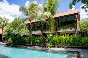 a woman walking by a swimming pool in front of a house at Arena Living in Sanur