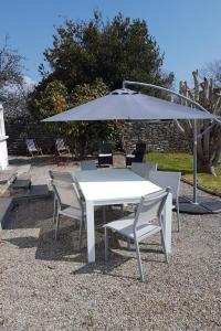 een witte tafel en stoelen onder een paraplu bij Les Camélias in Loctudy