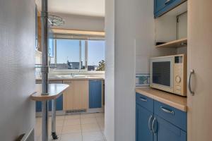 cocina con armarios azules, microondas y fregadero en Face au port, appartement pour 4 personnes, en Le Pouliguen