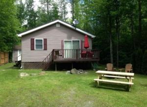 a house with a deck and a picnic table in the yard at Augur Lake Cabin Escape in Au Sable Forks