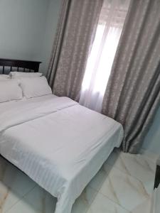 Una cama con sábanas blancas y una ventana con cortinas. en Cozy Apartment in Kololo en Kampala
