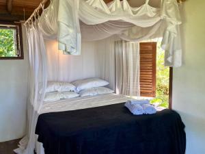a bed with white curtains and two towels on it at Casa Indigo Sargi - Bangalô, Chalé e Suite anexa in Uruçuca