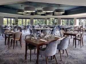 uma sala de jantar com mesas, cadeiras e janelas em Delta Hotels by Marriott St Pierre Country Club em Chepstow