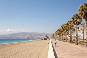 2 personnes marchant sur une plage bordée de palmiers dans l'établissement Nueva Almería beach & chill, à Almería