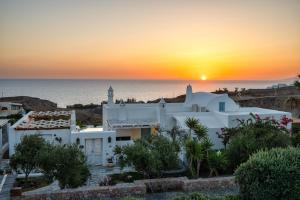 a sunset over a white house with the ocean in the background at Anema Boutique Hotel & Villas Santorini in Vourvoúlos
