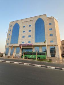 ARAEK AL KHLOOD HOTEL في مكة المكرمة: مبنى فيه باص أخضر يوقف امامه