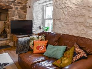 a brown leather couch with pillows in a living room at Bridge Cottage in Porkellis