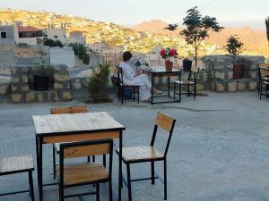 a man sitting at a table with tables and chairs at Treasury Terrace Apartments in Wadi Musa