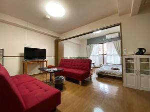a living room with a red couch and a bed at Laforet Tokaichi in Hiroshima