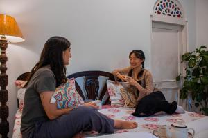 two women sitting on a bed talking at Anandmai Heritage Homestay in Jaipur