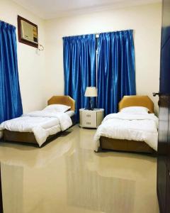two beds in a room with blue curtains at TWO BEDROOM FULLY FURNISHED APARTMENTS in Salalah