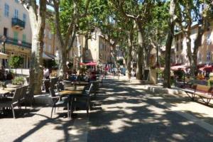 une rue de la ville avec des tables, des chaises et des arbres dans l'établissement Au coeur du Village, à Cotignac