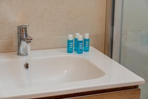 a bathroom sink with three blue bottles on it at Hotel Portoconte in Porto Conte