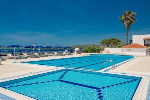 a large swimming pool with chairs and umbrellas at Hotel Portoconte in Porto Conte