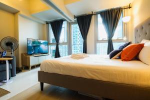 a bedroom with a large bed with windows and a television at Cozy 1BR Apartment in Manila, BGC, with Balcony & Pool in Manila