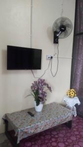 a living room with a table and a tv and flowers at Tina Homestay Budget in Ketereh