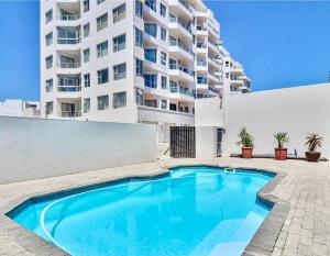 a swimming pool in front of a tall building at Abode Africa in Bloubergstrand