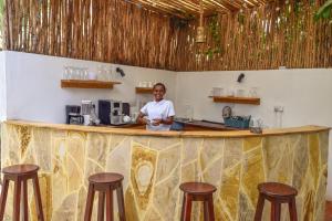 a man standing behind a bar with stools at Barabara house in Jambiani