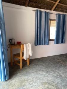 um quarto com cortinas azuis, uma mesa e uma janela em Kokopelli Bungalows em Nungwi