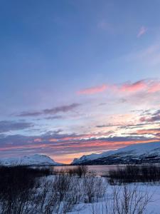 a sunset over a snowy field with mountains in the background at Modern apartment nearby city centrum in Tromsø