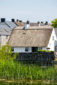 an old house with a thatched roof next to the water at Michaeleen's Manor B&B in Cong