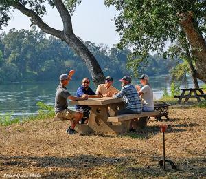a group of people sitting at a picnic table by a lake at Three Bedroom River Access in Redding