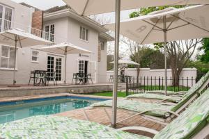 una piscina con sillas y sombrillas junto a una casa en Rozenburg Guest House, en Stellenbosch