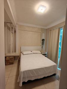 1 dormitorio con cama blanca y ventana en Apartamento Centro Bombinhas, en Bombinhas