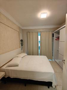 Un dormitorio con una gran cama blanca y una ventana en Apartamento Centro Bombinhas, en Bombinhas